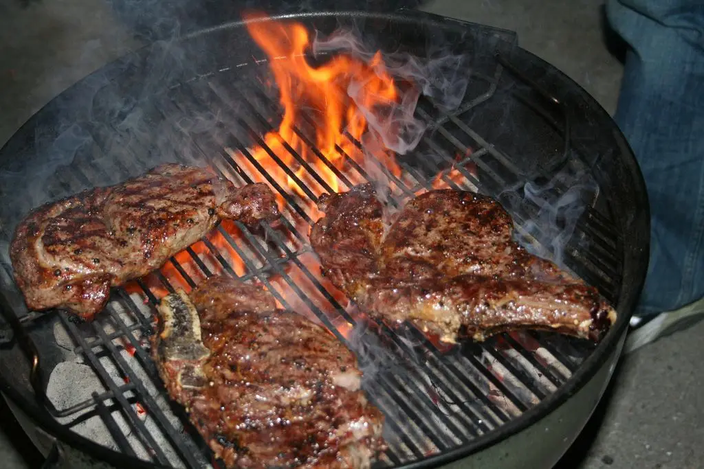 Steaks searing on a grill over open flame