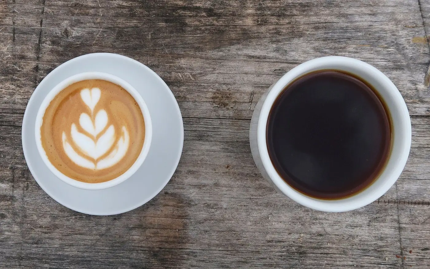 A latte with leaf art beside a cup of black coffee