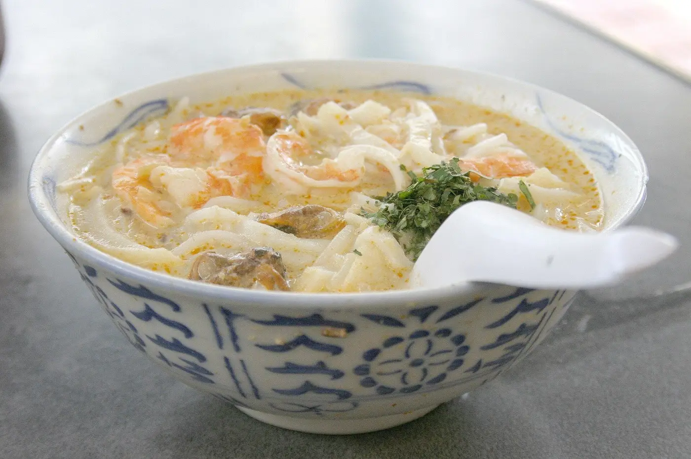A bowl of laksa with cockles, prawns and cut noodles in coconut gravy