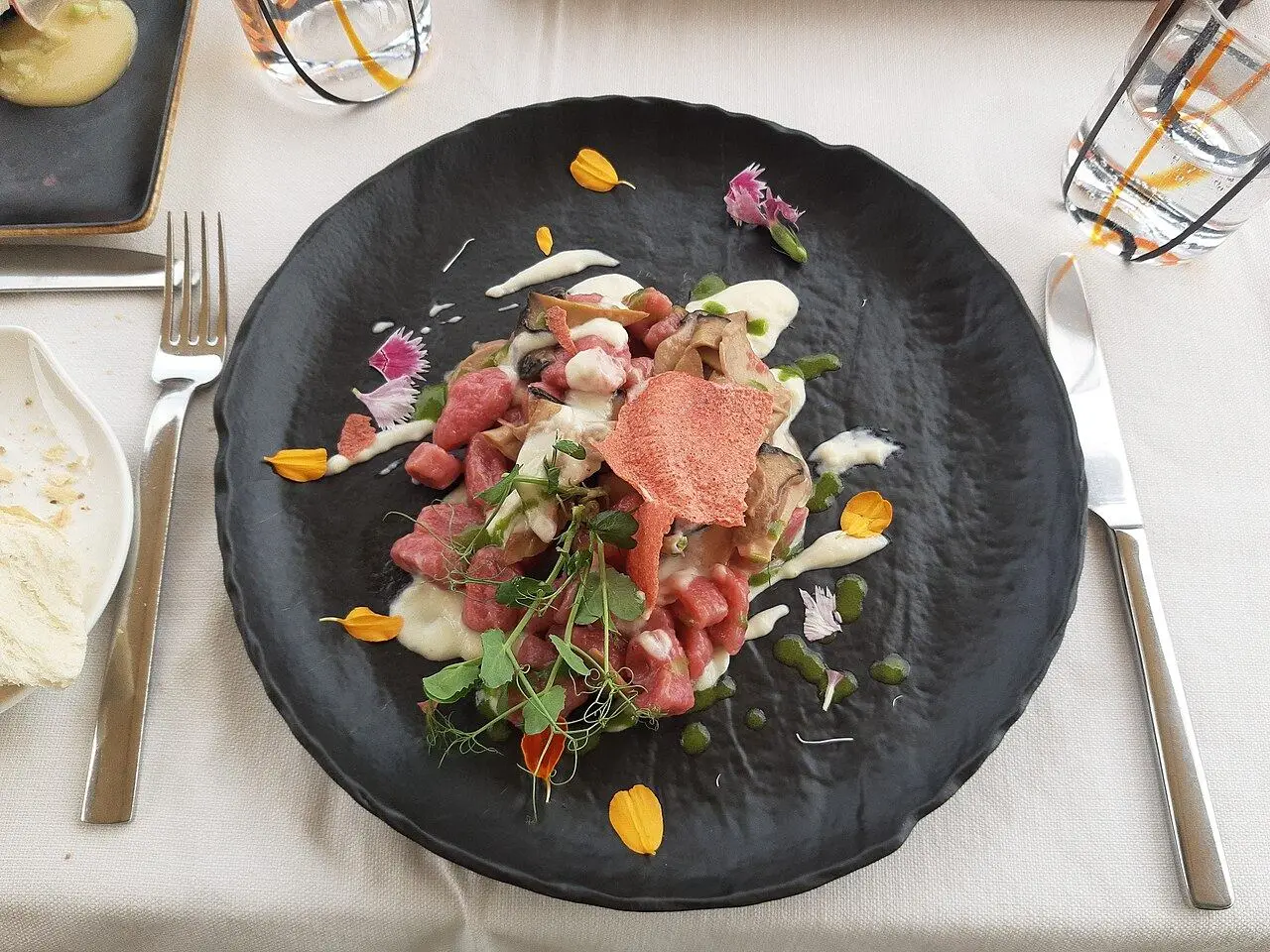 A plated course with flowers and herbs on a dark stone plate